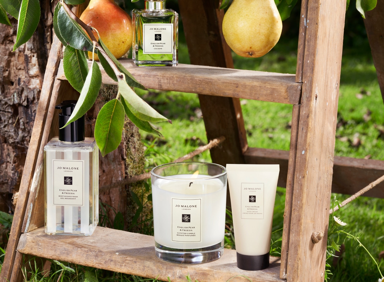 Adwoa Aboah with braided hair, biting into a pear with backdrop of three large pear props placed on top of a car roof rack.